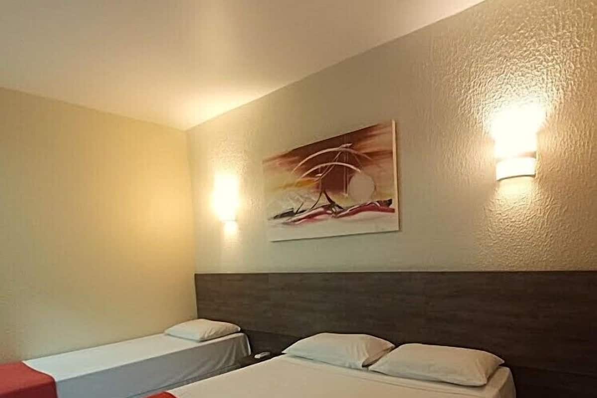 Une chambre d’hôtel avec deux lits, une couverture rouge sur le lit de gauche et un tableau au mur.