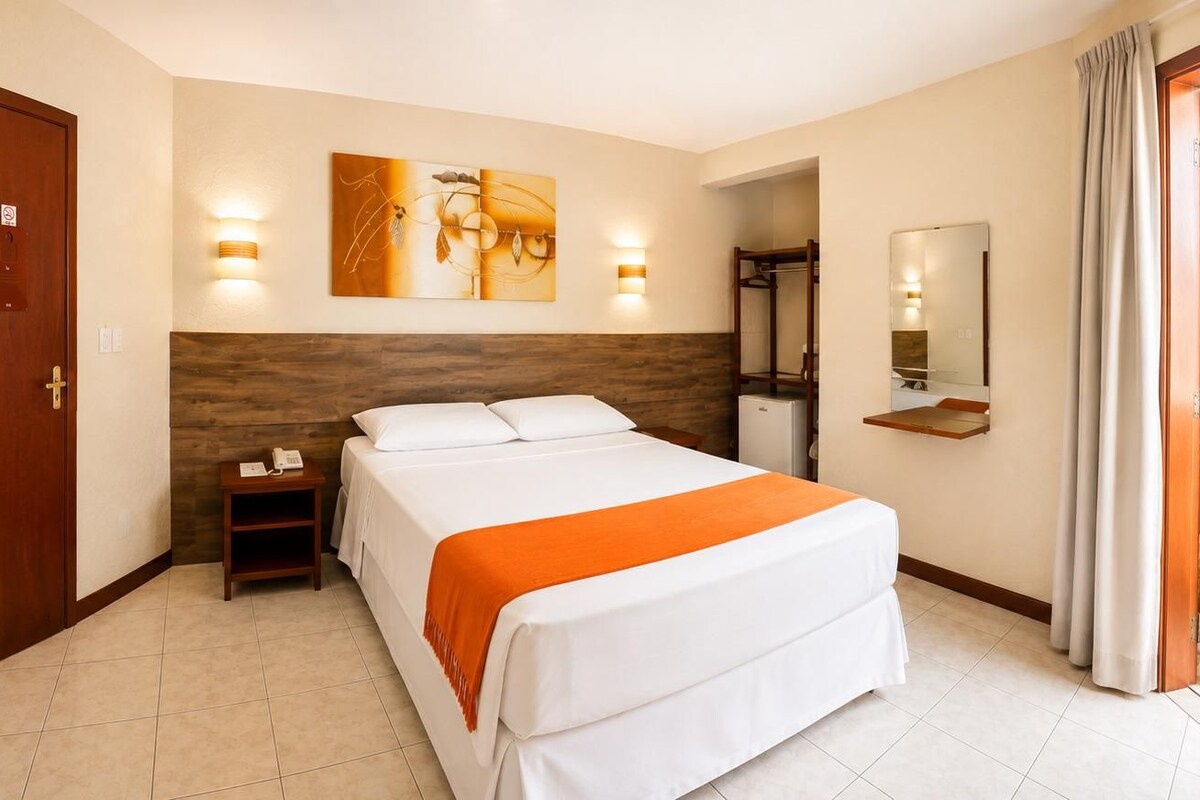 Een hotelkamer met een bed, een televisie, een schilderij en een badkamer zichtbaar door een geopende deur.
