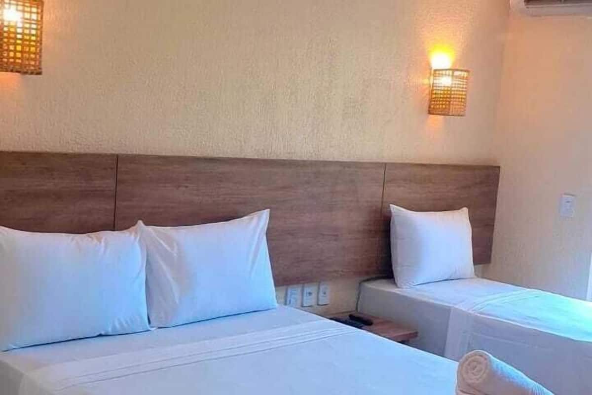 Une chambre d’hôtel avec deux lits, chacun agrémenté de draps et d’oreillers blancs, une couverture rouge sur le lit de droite et des lampes fixées au mur.
