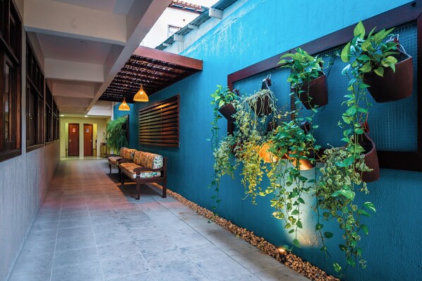 A hallway with a blue wall, wooden bench, hanging plants, and a tiled floor. - Ayla Praia Hotel (Porto Seguro)