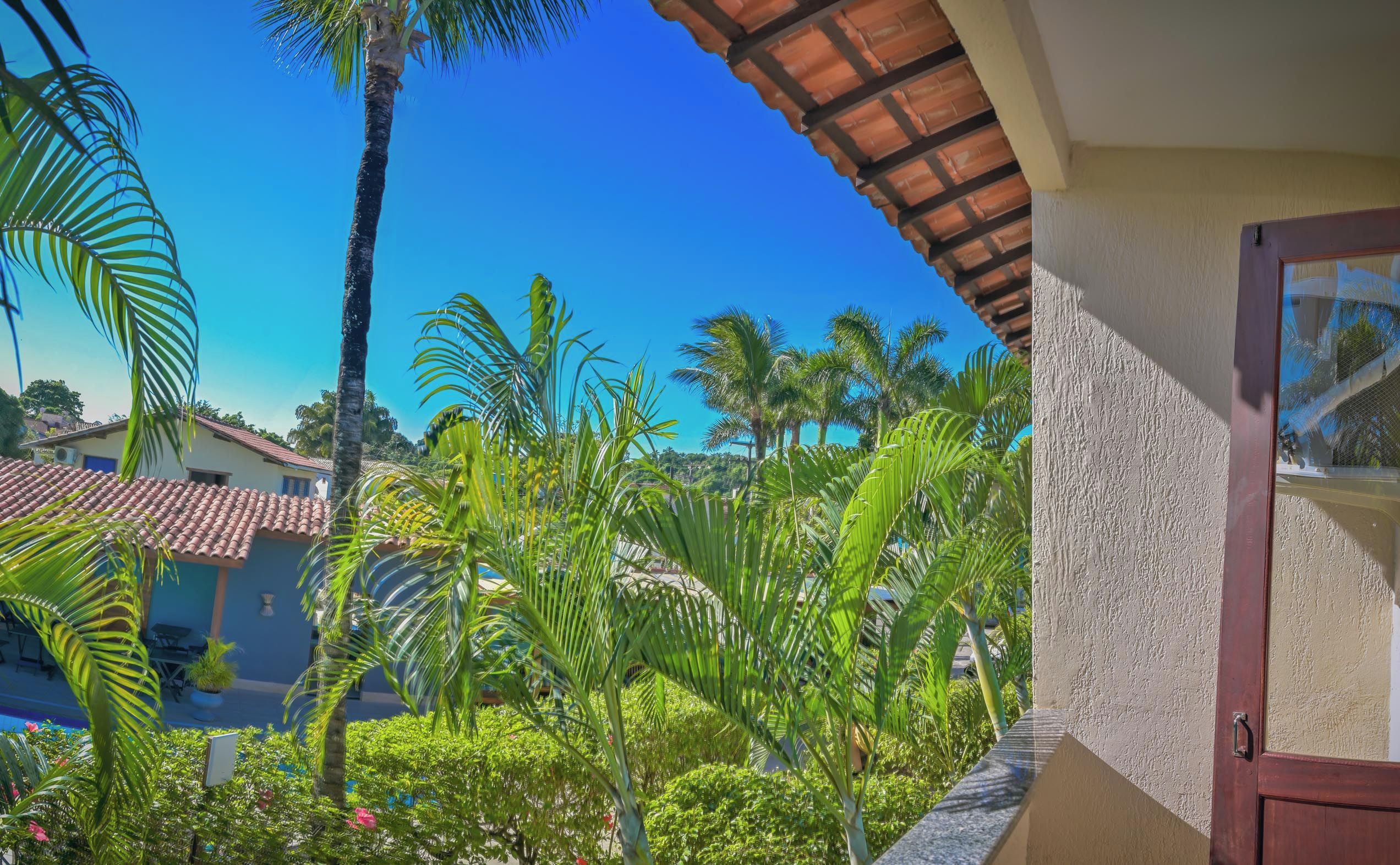 A view of a building with a tiled roof, surrounded by lush greenery and palm trees.