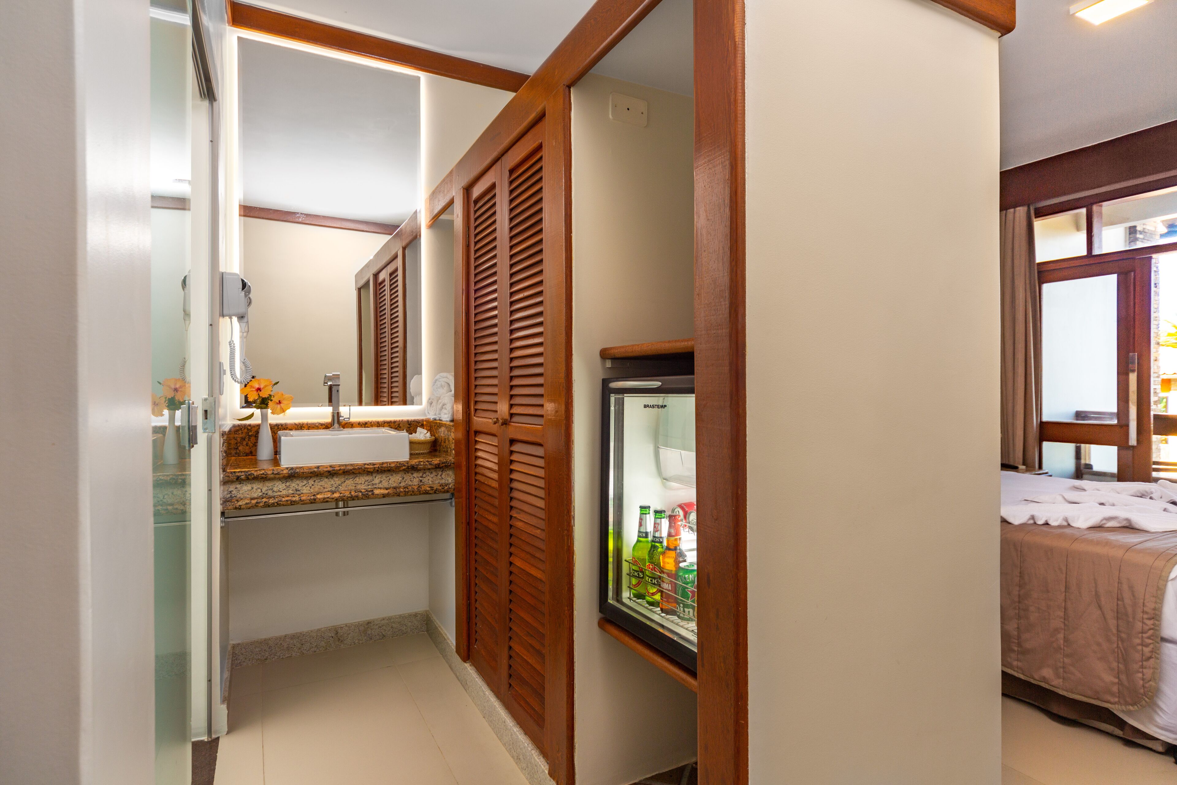 A bathroom with a glass shower enclosure, a wooden door, and a refrigerator with beverages.