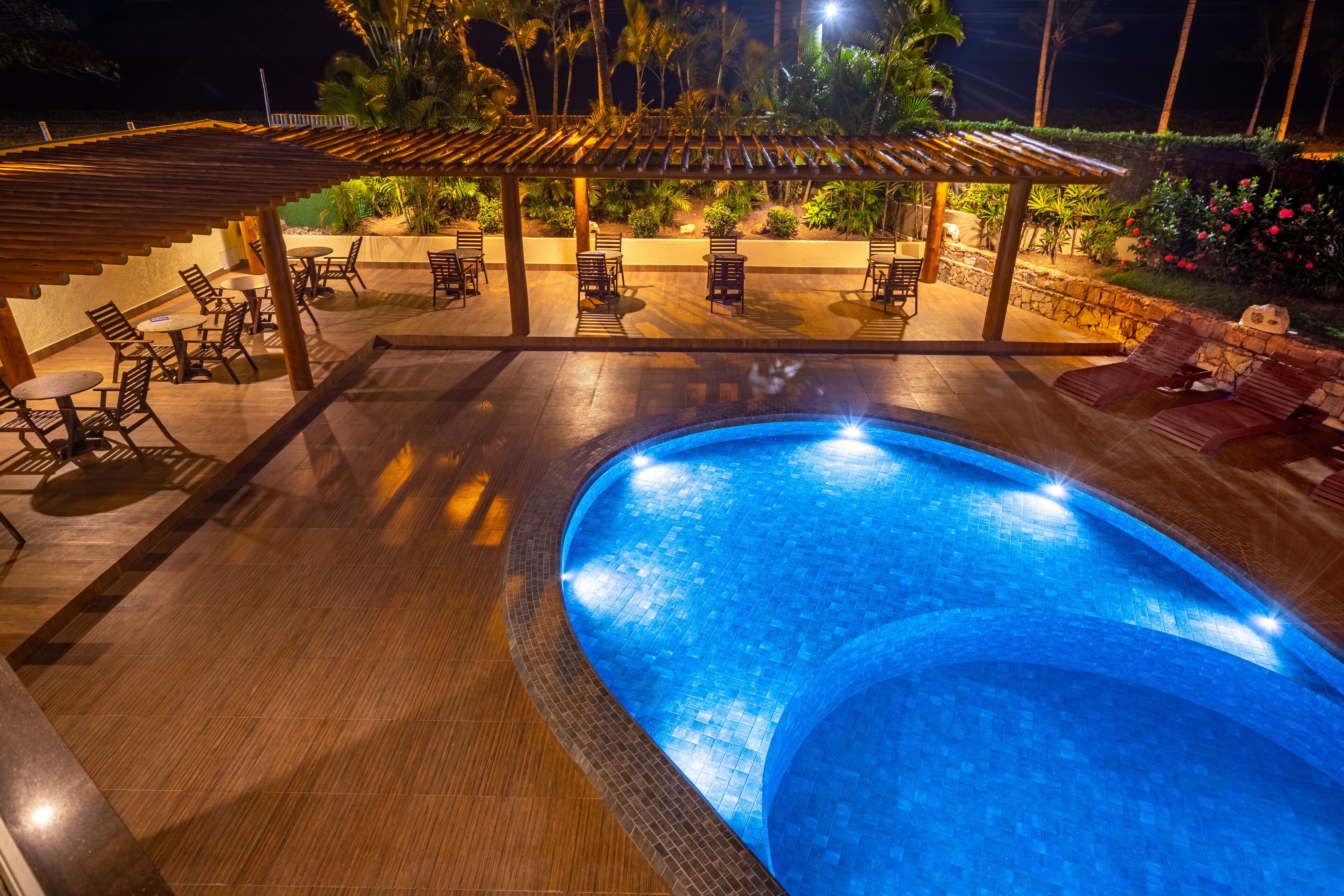 Zona de piscina con un porche de madera, asientos y una pared de piedra.