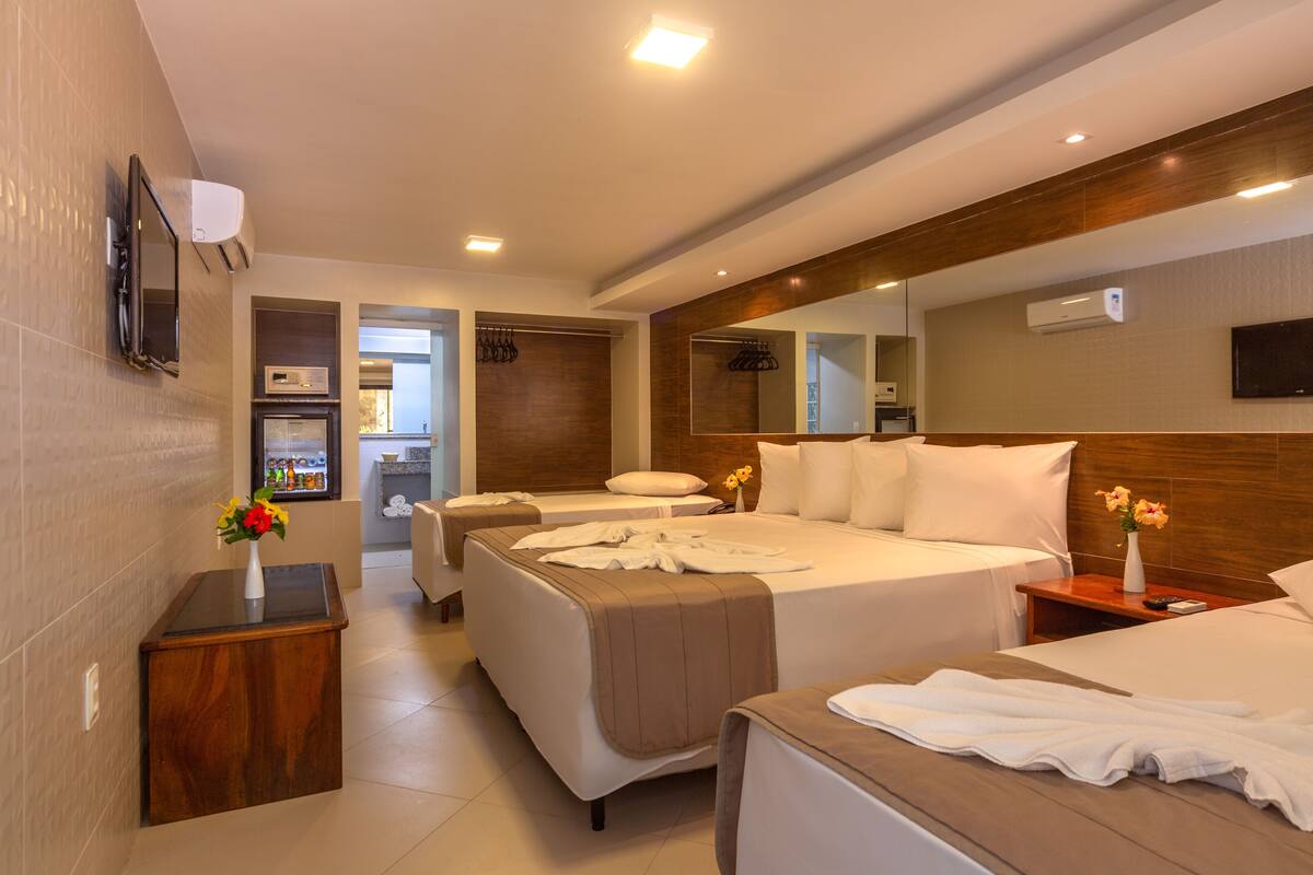 A modern hotel room with two beds, a wooden headboard, a flat-screen TV, a minibar, and a bathroom visible through an open door.