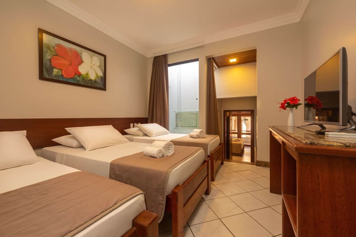 A hotel room with three beds, a wooden desk, a television, and a painting on the wall.