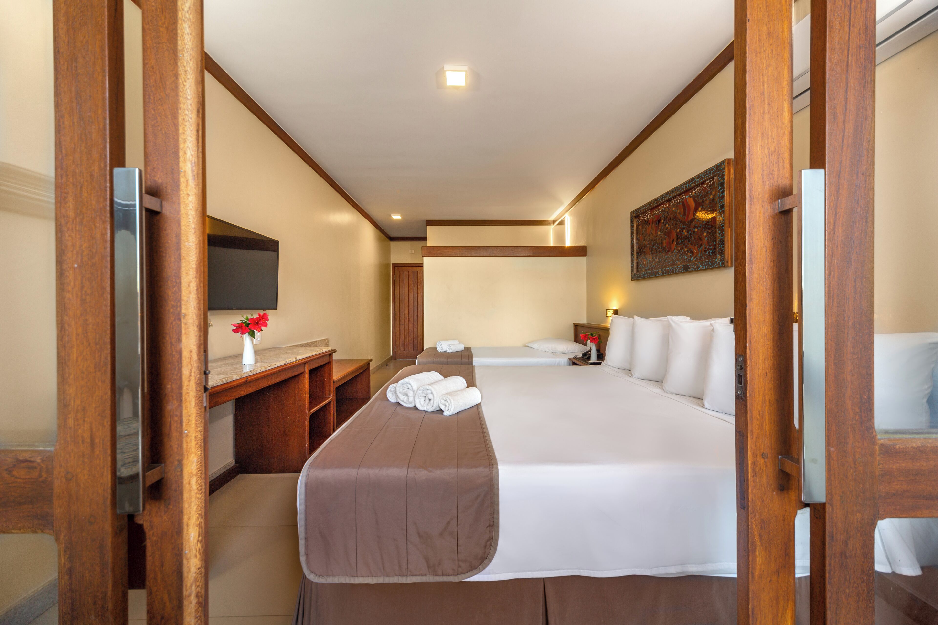 A hotel room with a bed, a desk, a chair, a TV, and a painting on the wall.