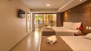 A hotel room with a large bed, a TV mounted on the wall, and a view of a garden through a glass door. - Quinta do Sol Praia Hotel (Porto Seguro)
