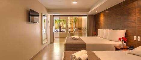 A hotel room with a large bed, a TV mounted on the wall, and a view of a garden through a glass door.