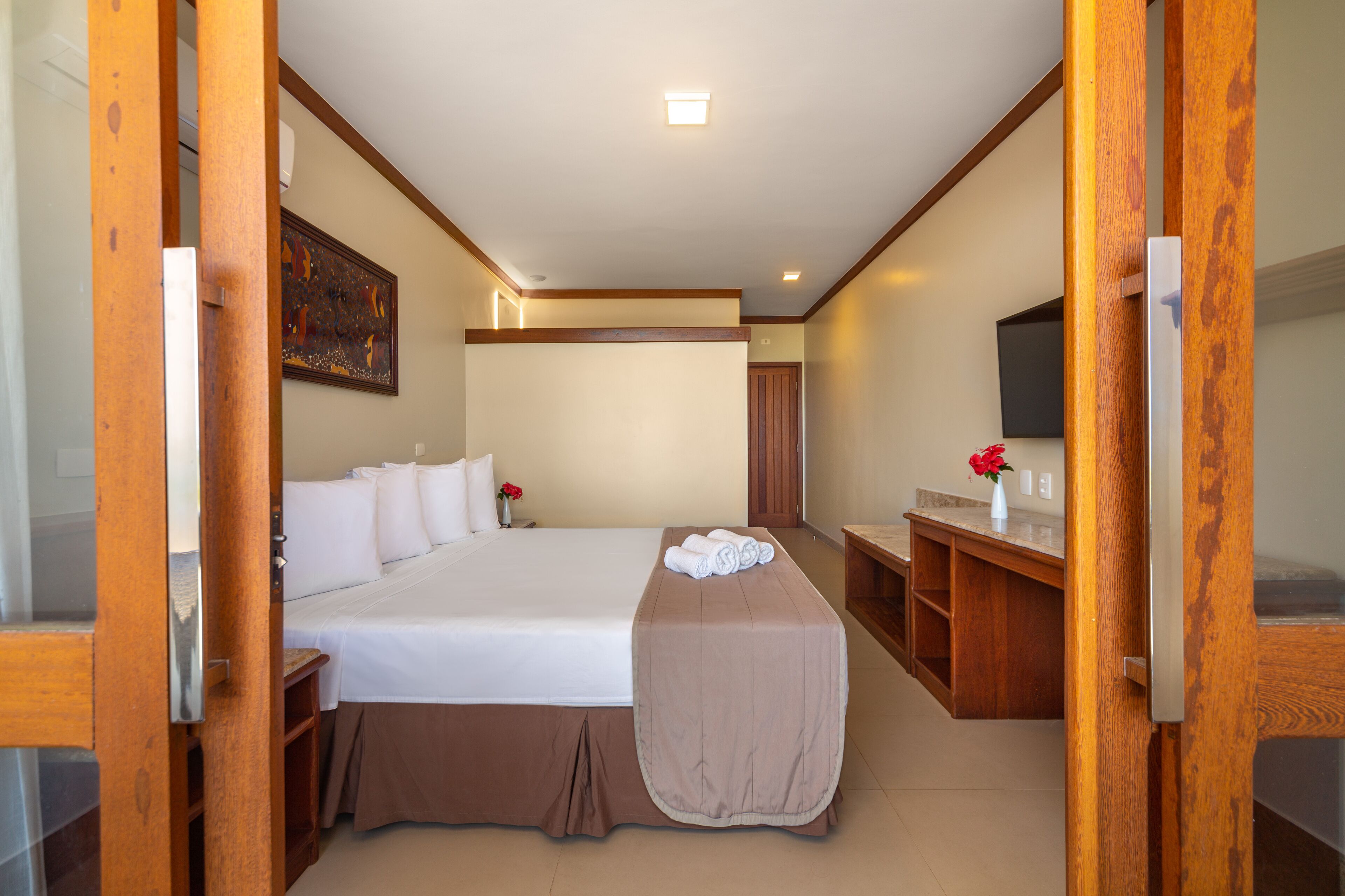 Une chambre d’hôtel avec un grand lit, une table de chevet, un bureau avec une chaise, un téléviseur à écran plat et un tableau au mur.