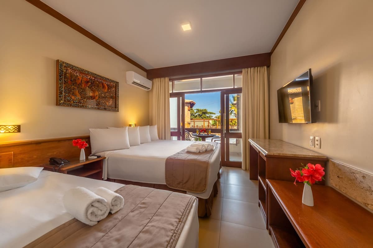 A hotel room with two beds, a TV, a balcony with a view, and a painting on the wall.