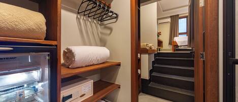 A hotel room with a minibar, a towel rack, a wooden shelf with towels, and a staircase leading to another room.