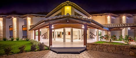 A modern hotel entrance with a covered patio, stone pillars, and a well-lit facade.