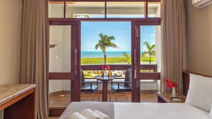 A hotel room with a large bed, a small table with drinks, two chairs, and a balcony with a view of the ocean. - Quinta do Sol Praia Hotel (Porto Seguro)
