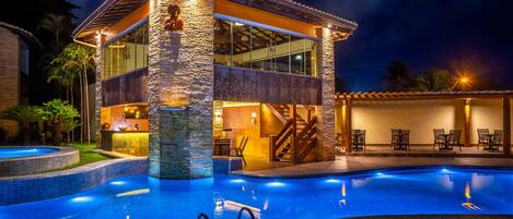A modern poolside area with a stone structure, a glass-enclosed lounge, and a well-lit pool.