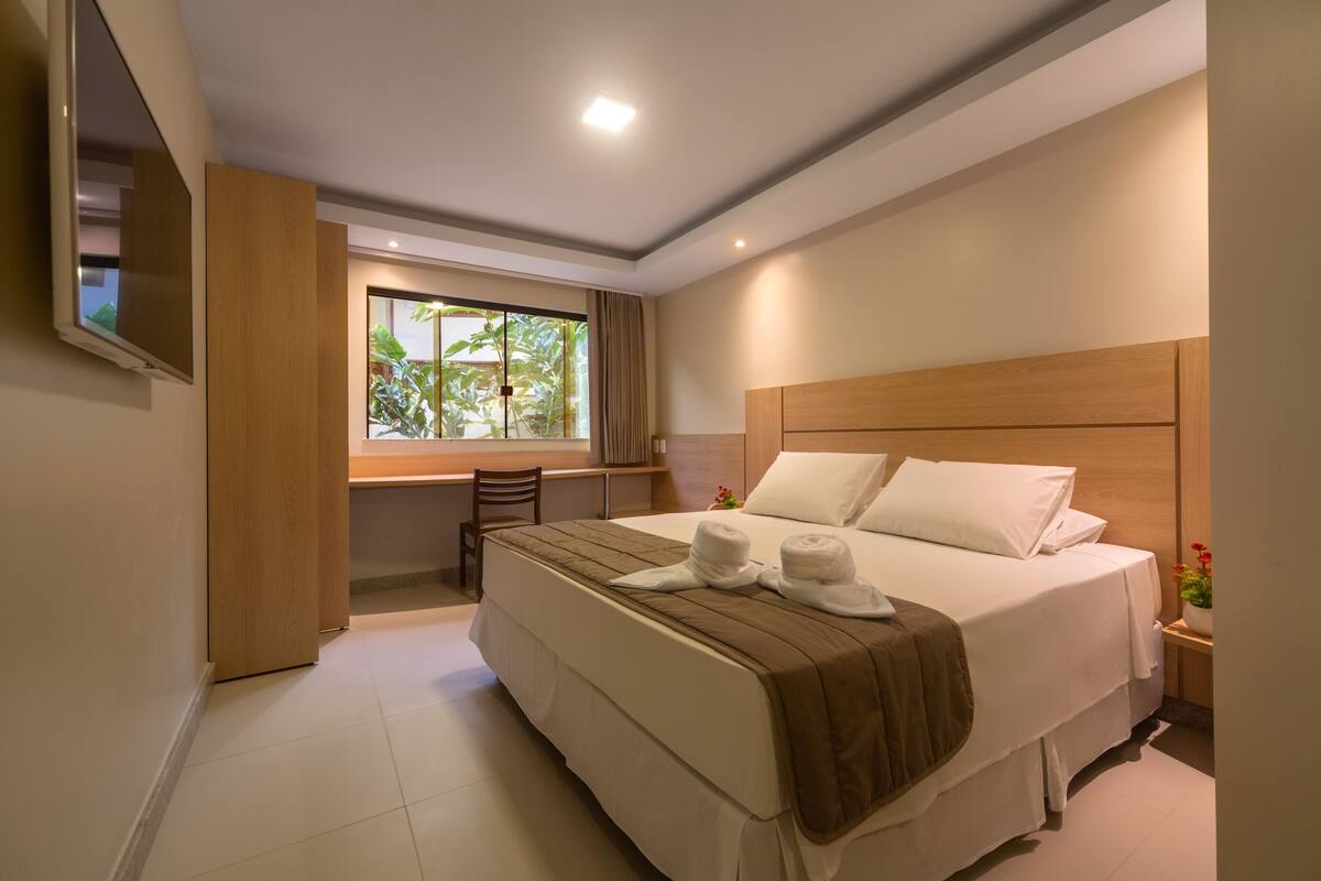 A hotel room with a large bed, a desk, and a TV mounted on the wall.