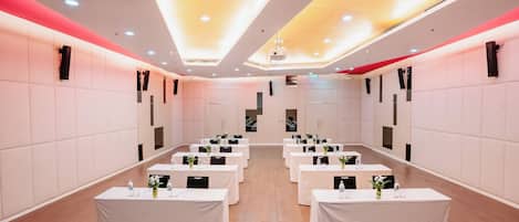 A conference room with multiple tables, white tablecloths, and ceiling lights.