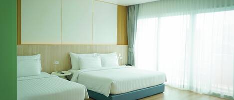 A hotel room with two beds, a bedside table, a nightstand, a power outlet, and a window with curtains.