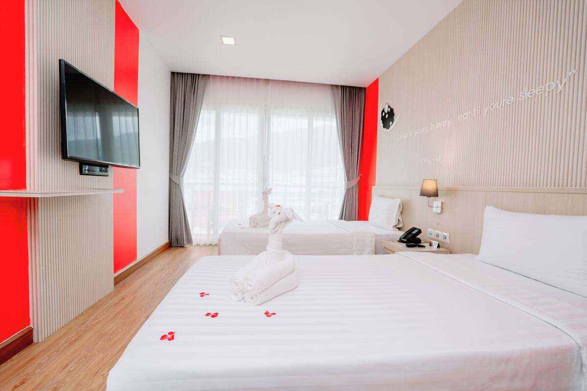 Hotellihuone, jossa on suuri sänky, seinälle asennettu televisio ja yöpöytä, jossa on lamppu.