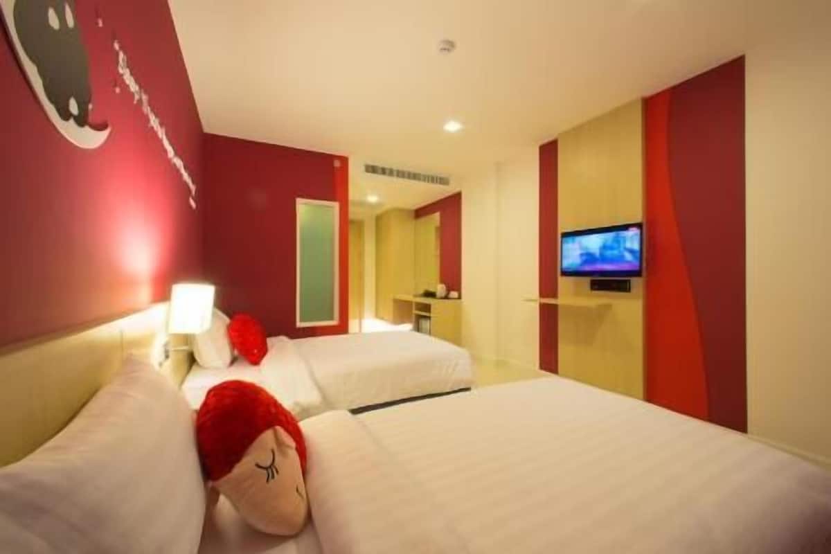 Hotellihuone, jossa on kaksi sänkyä, televisio, peili ja punainen seinä.