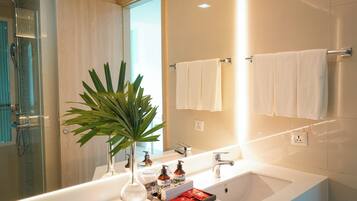 Une salle de bain moderne avec une douche à parois de verre, un grand miroir et un lavabo blanc agrémenté d’articles de toilette.