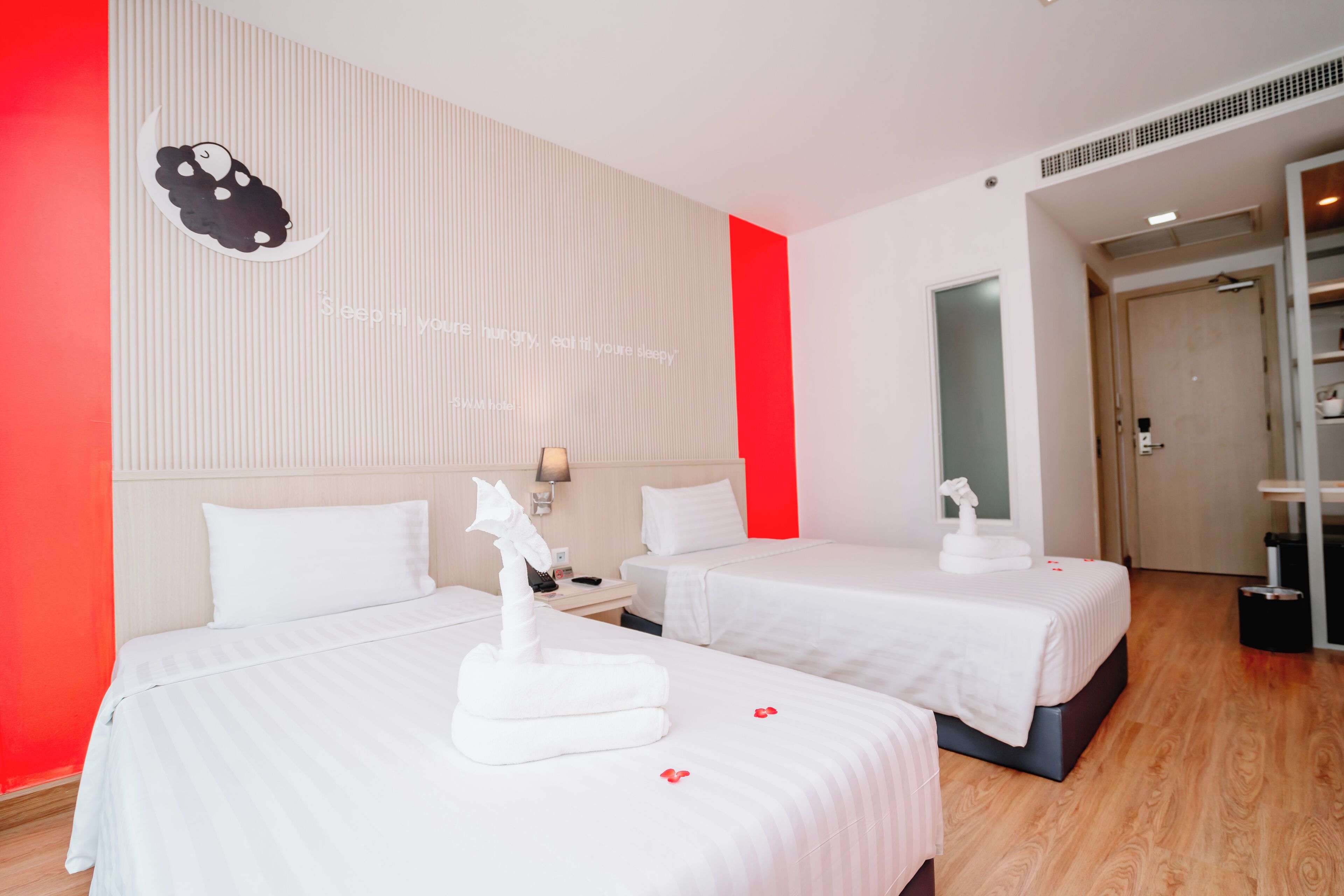 Une chambre d’hôtel avec deux lits, un mur d’accent rouge et une œuvre d’art décorative.