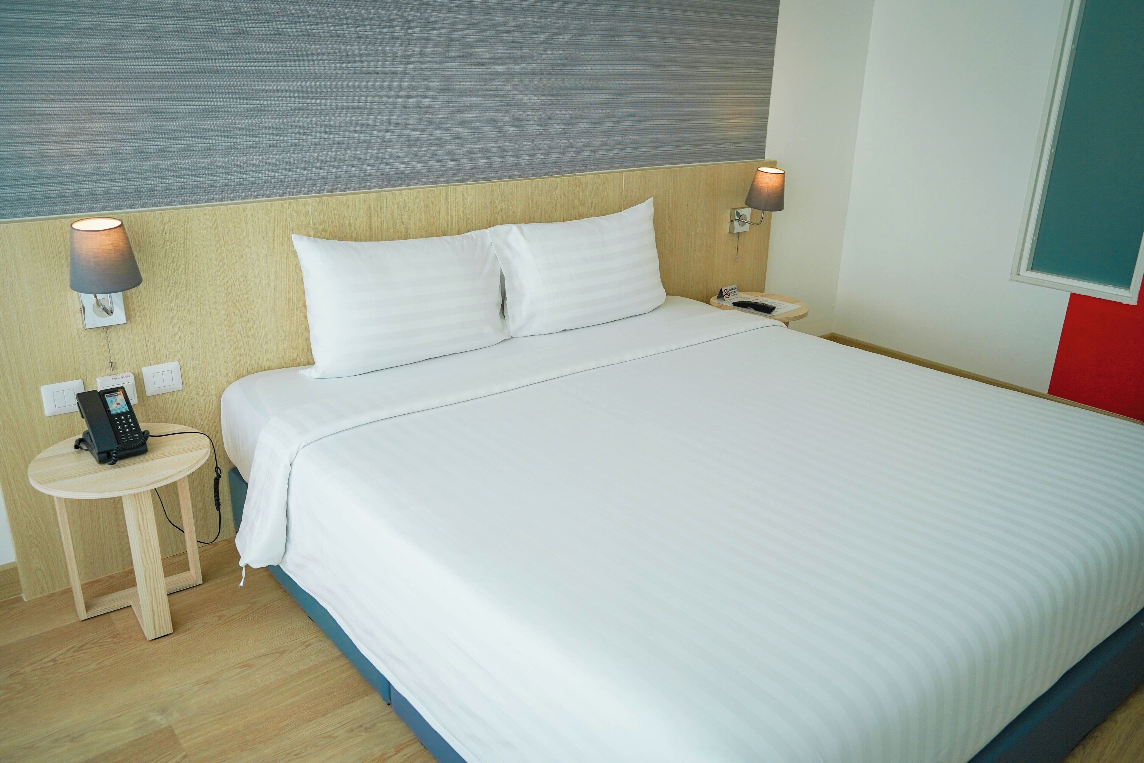 A hotel room with a bed, bedside lamps, a telephone, and a small table.