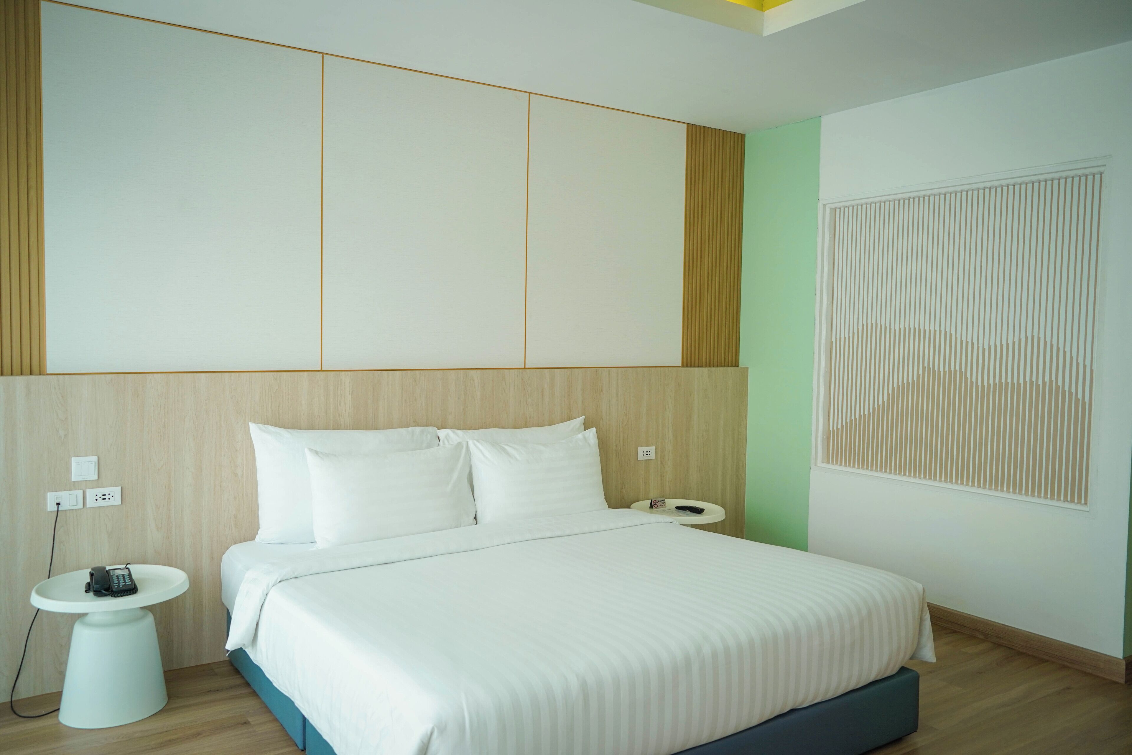A modern hotel room with a large bed, a bedside table, and a wall-mounted telephone.