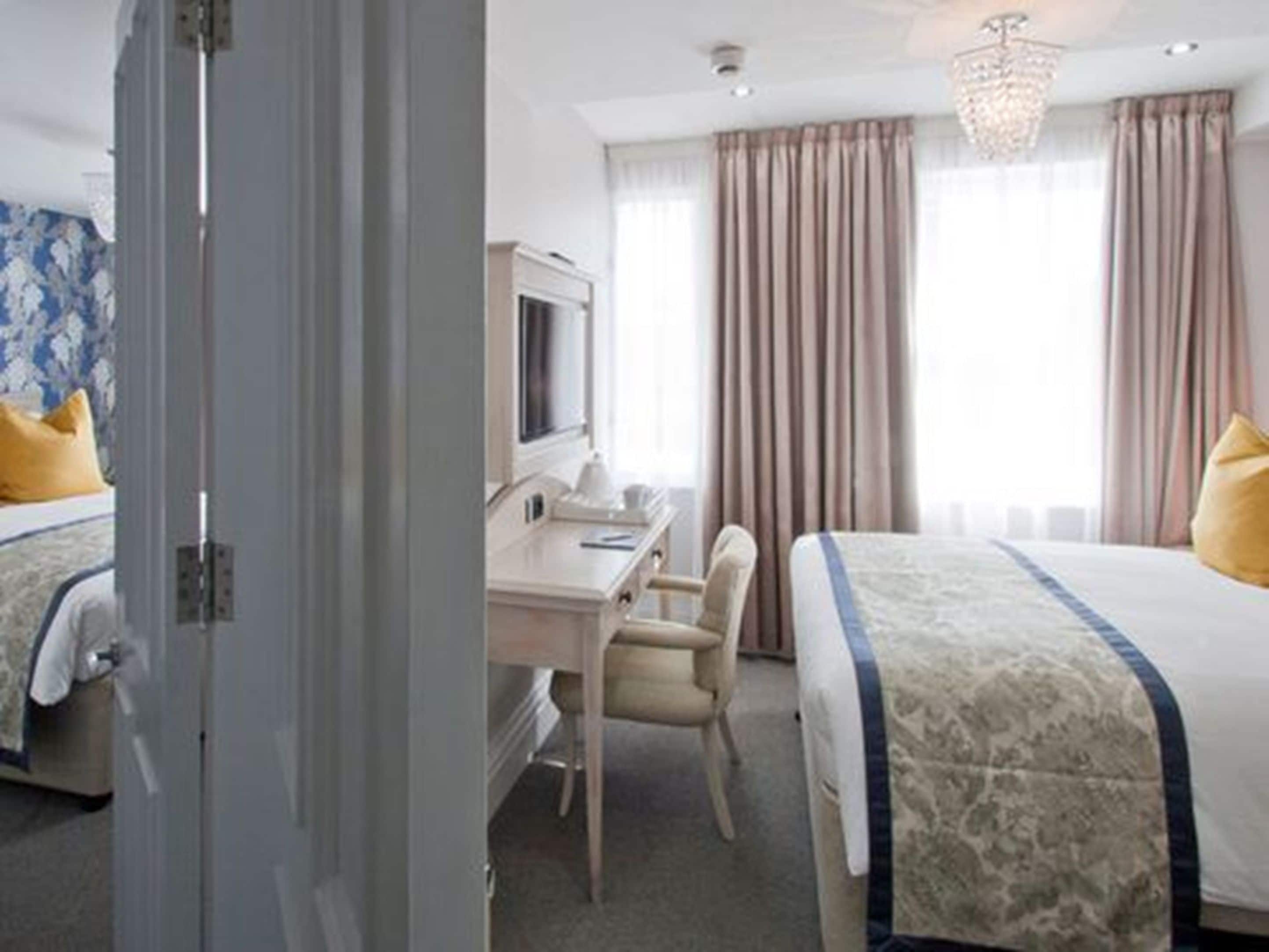 A hotel room with two beds, a desk, a chair, a television, and a chandelier.