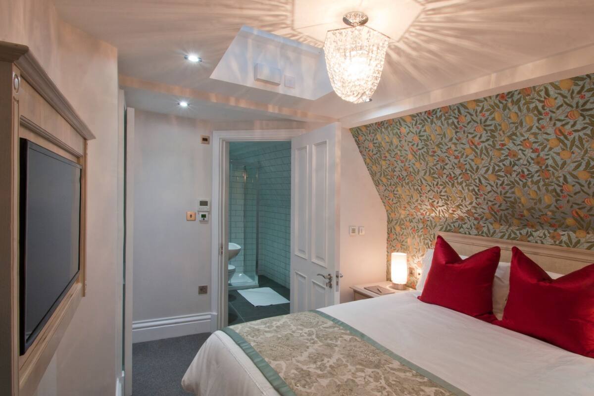 A hotel room with a bed, a shower, a bathroom, and a nightstand with a lamp.