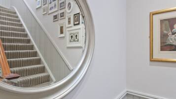 A staircase with a carpeted handrail, a wall with framed pictures, and a round mirror reflecting part of the room.