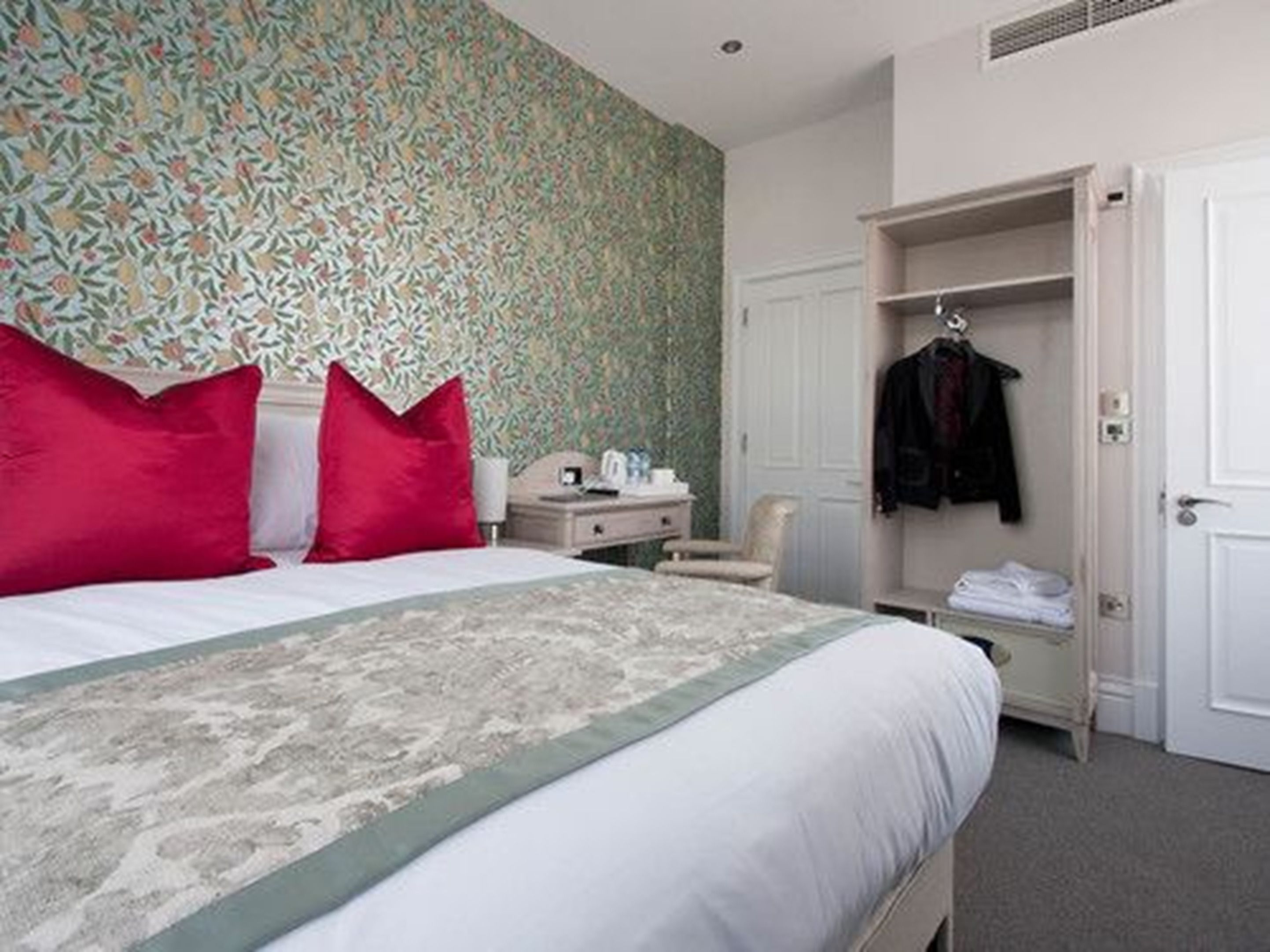 A neatly arranged hotel room with a bed, a bedside table, a chair, and a wardrobe.