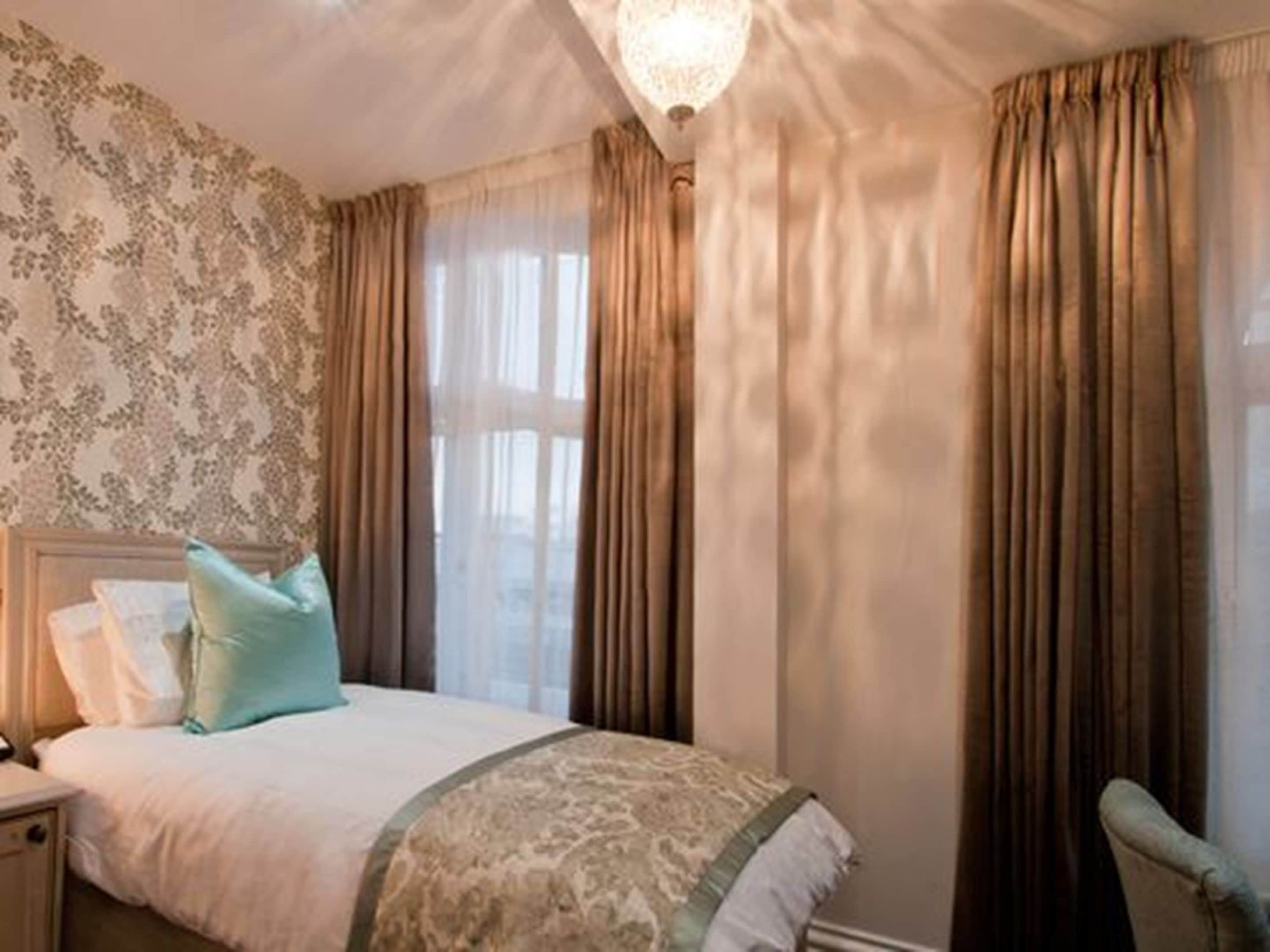 Une chambre à coucher avec un lit, une table de chevet, une chaise et une fenêtre avec des rideaux.