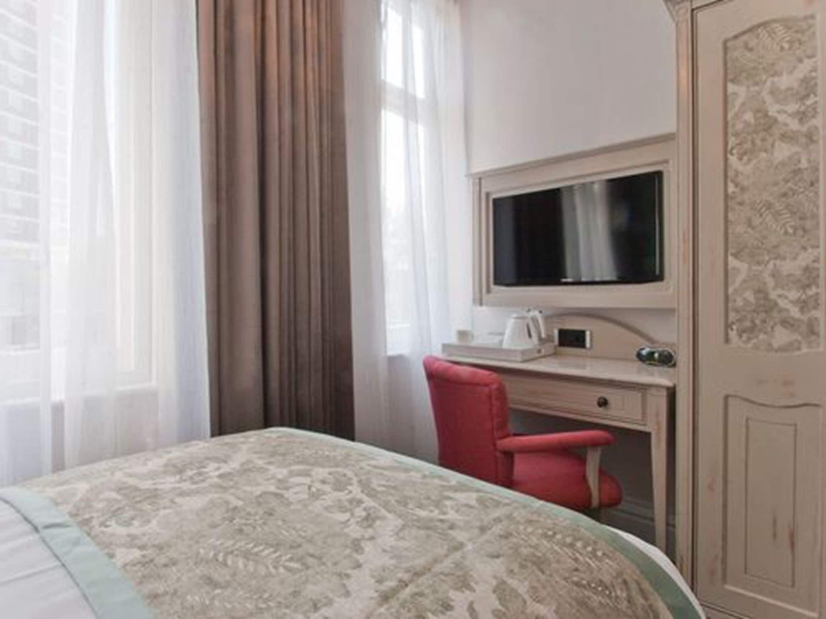 Een hotelkamer met een bed, een bureau met een computerscherm, een rode stoel en een kledingkast.