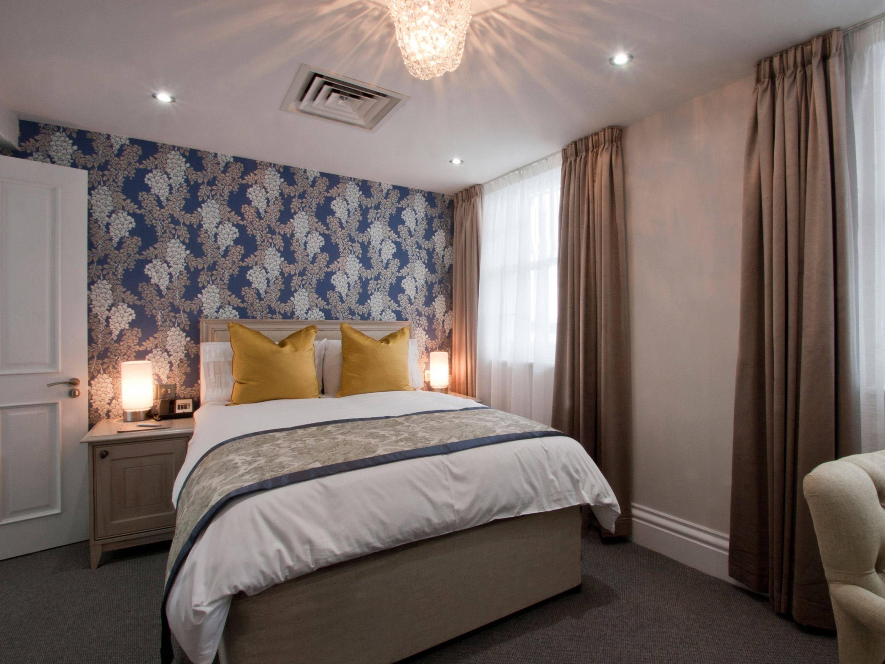 A bedroom with a large bed, a nightstand, a lamp, and a window with curtains.