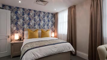 A bedroom with a large bed, a nightstand, a lamp, and a window with curtains.