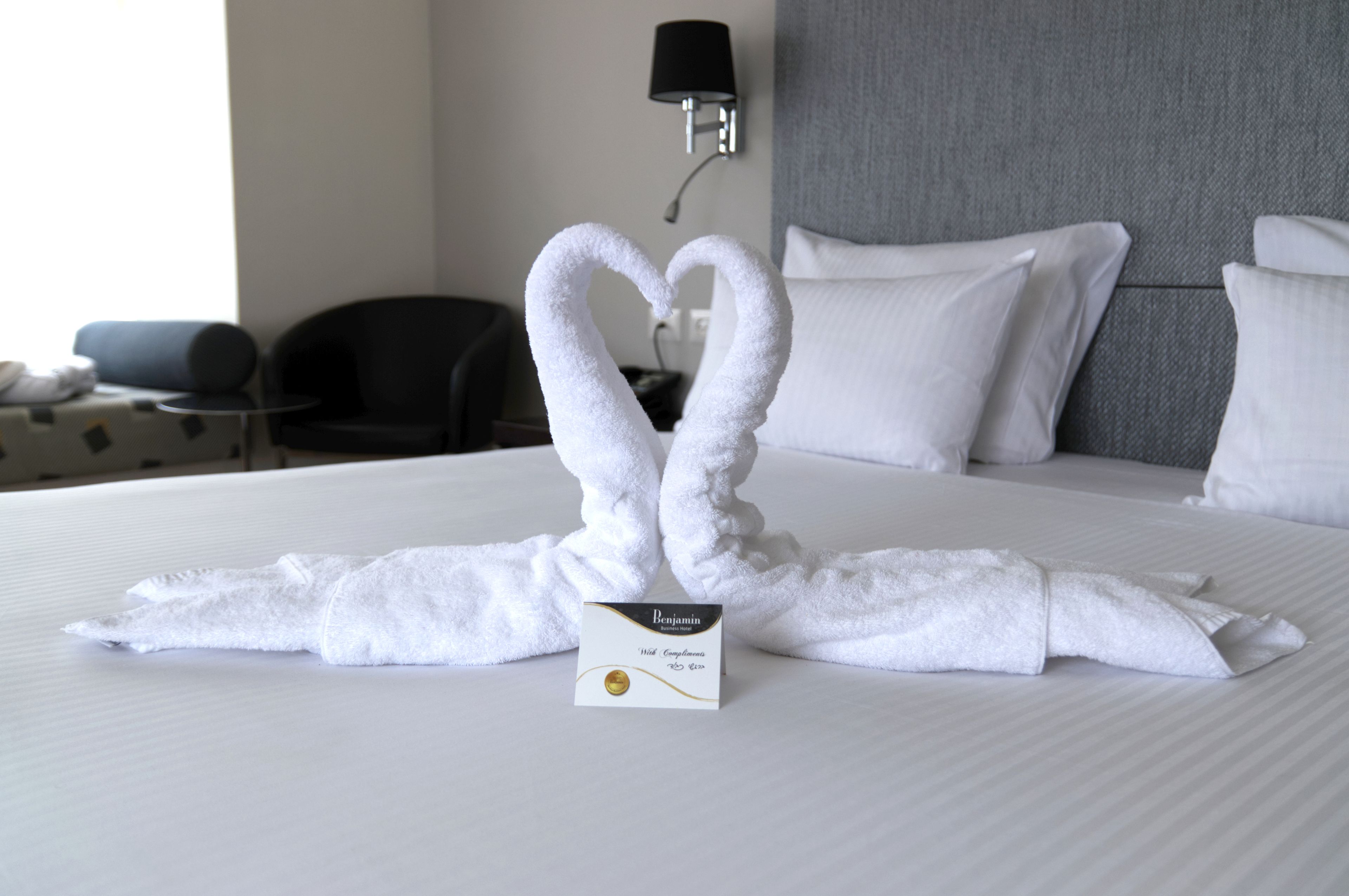 Un lit bien fait, agrémenté d’une serviette pliée en forme de cœur et d’une carte de l’hôtel Benjamin.