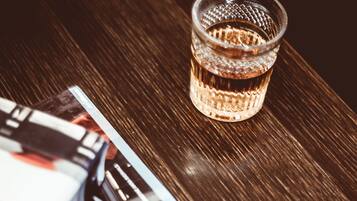 Una mesa de madera con un vaso de líquido ámbar, una baraja de cartas y un libro.