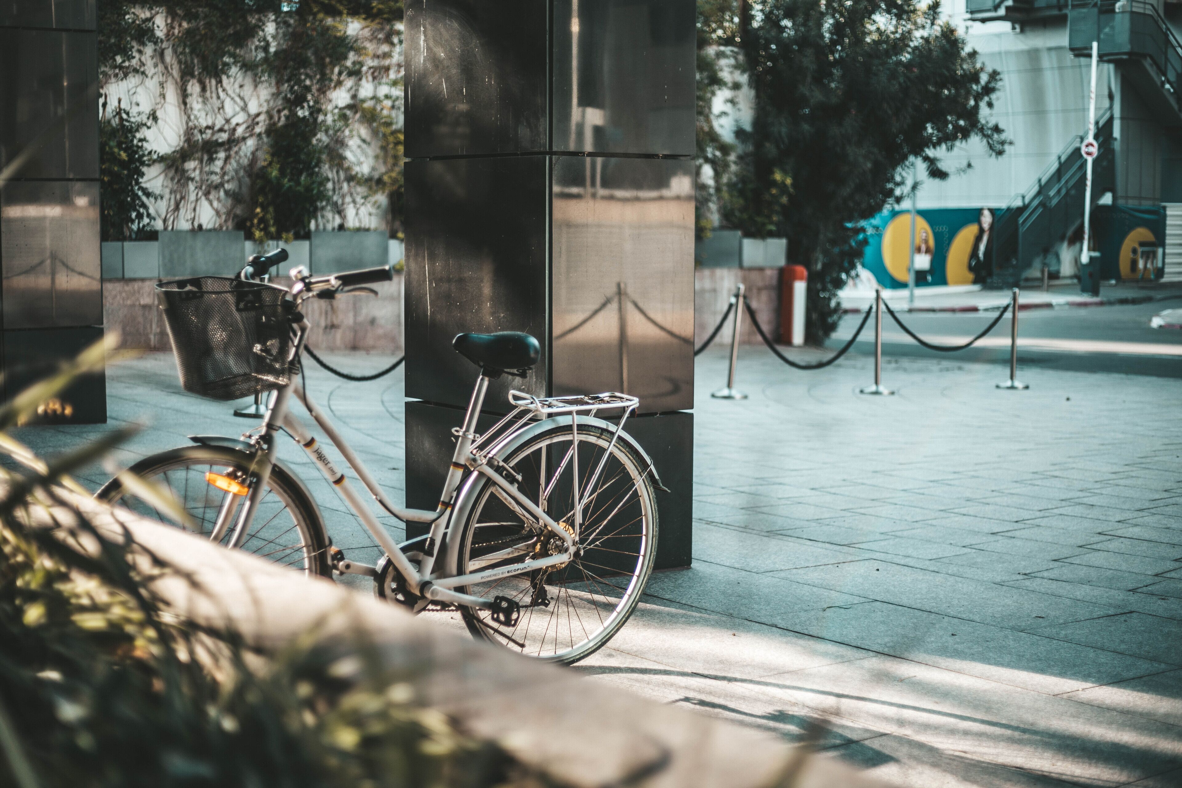 Una bicicleta estacionada junto a un pilar negro con una cesta metálica sujeta al manillar.