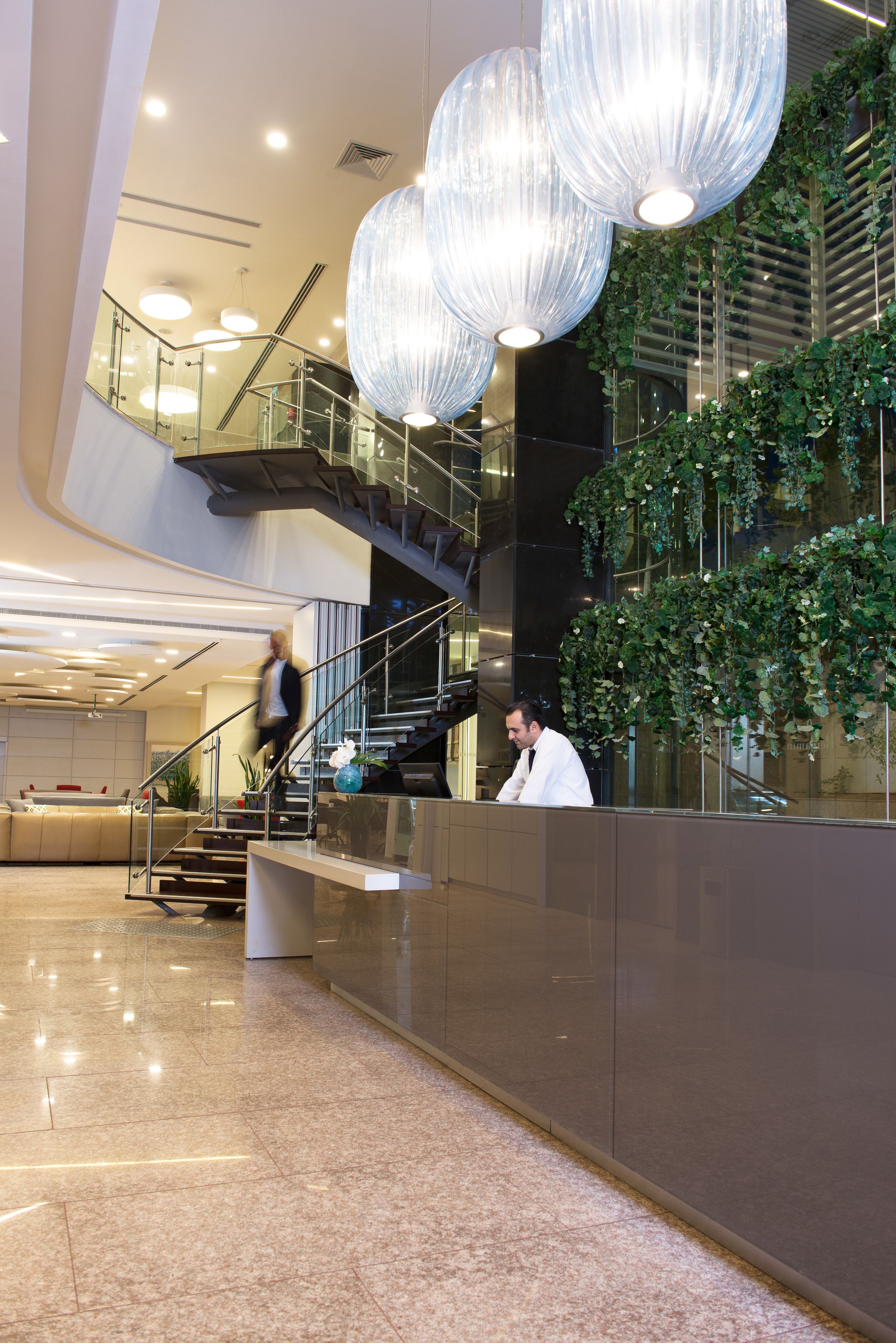A modern lobby with a glass staircase, a reception desk, and hanging pendant lights.