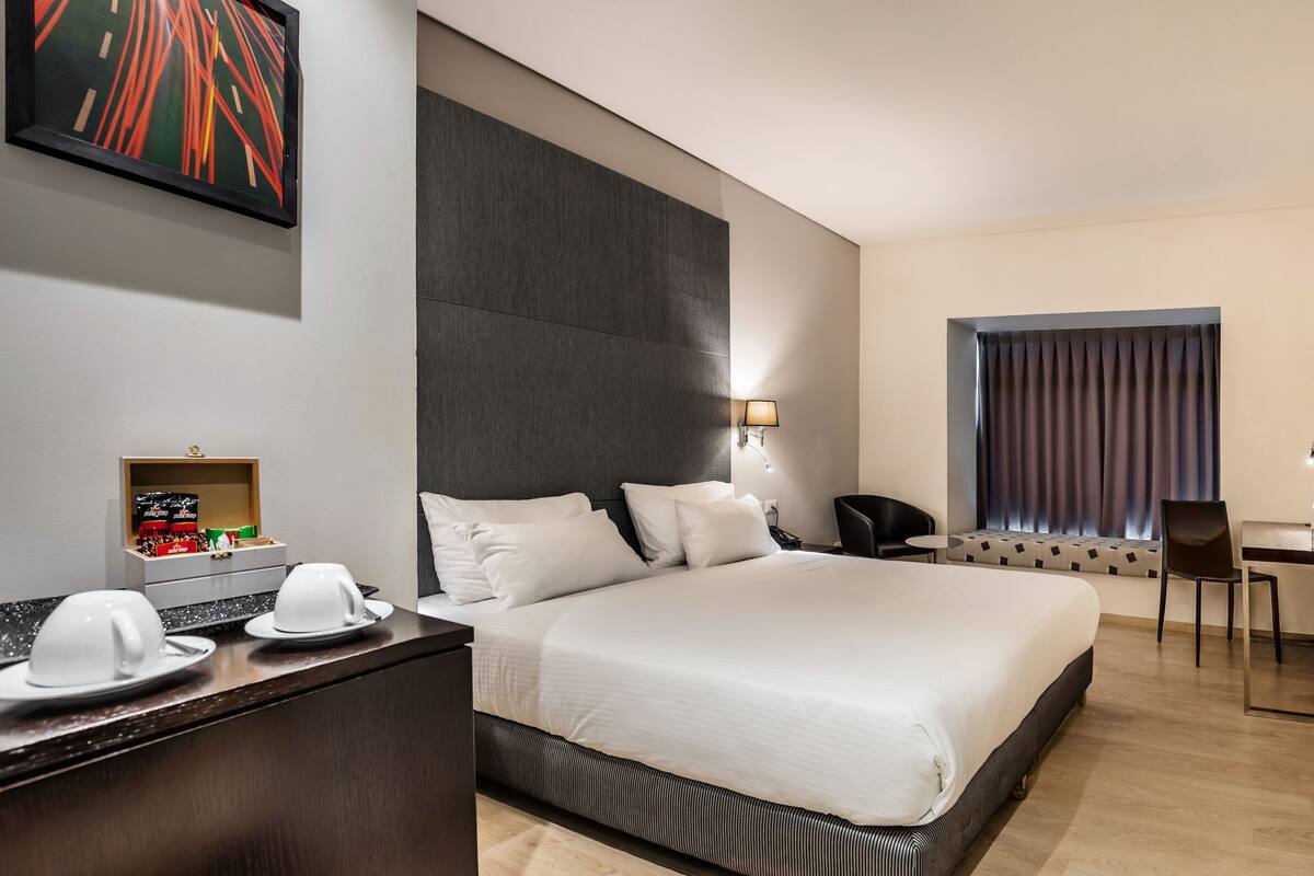 Une chambre d’hôtel moderne dotée d’un grand lit, d’un bureau, d’une chaise et d’un petit coin salon avec une fenêtre.