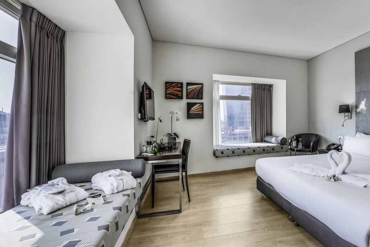 Une chambre d’hôtel moderne avec un grand lit, un petit canapé, un bureau avec une chaise, une fenêtre avec des rideaux et une vue sur la ville.