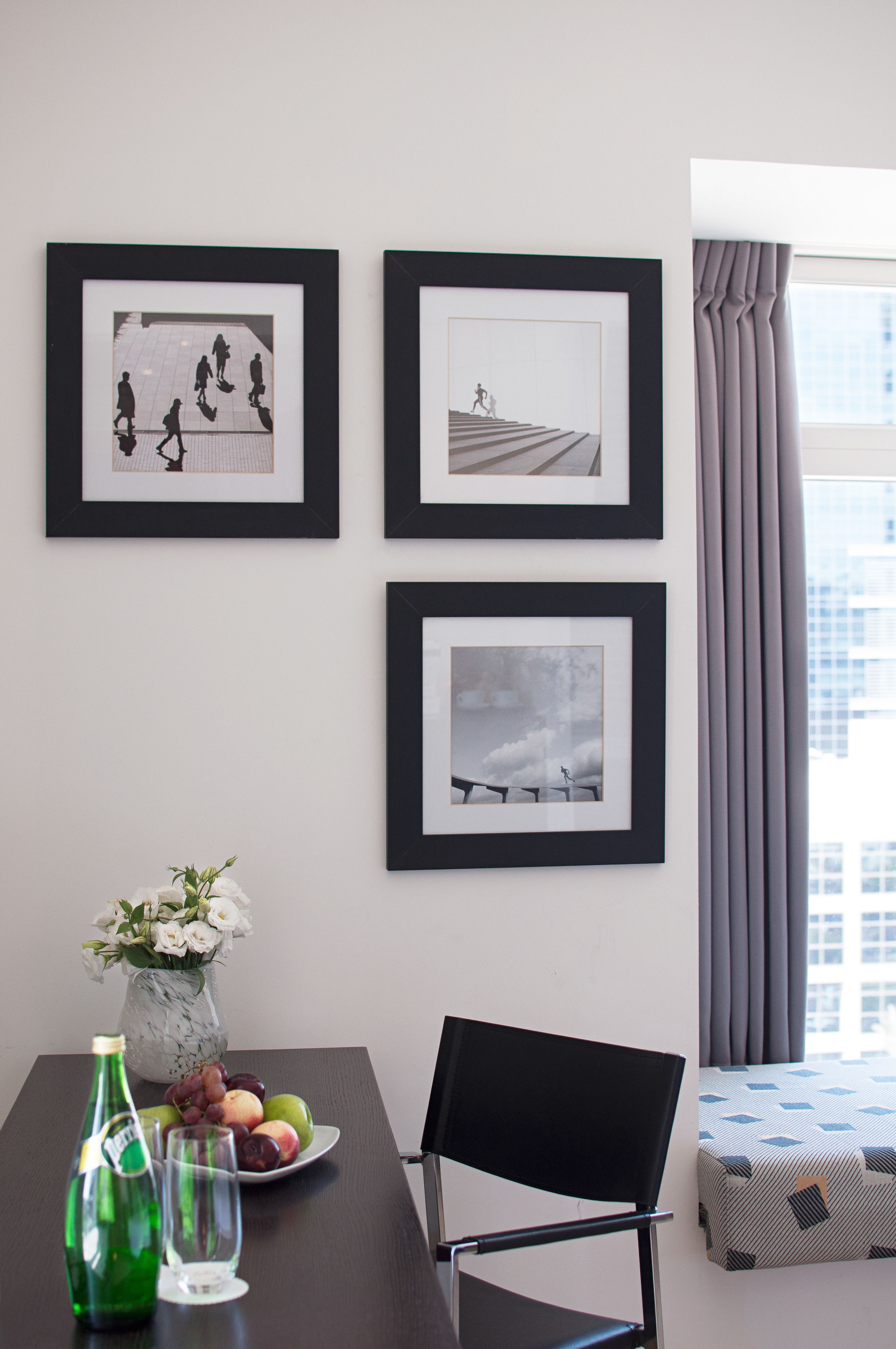 A modern room with a dining table, framed pictures on the wall, a vase with flowers, and a city view through the window.
