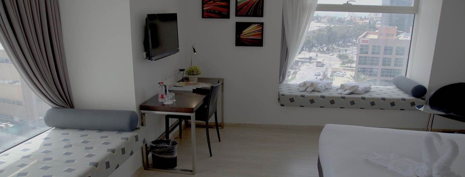 A hotel room with a bed, a desk, a chair, a TV, and a window with a city view.