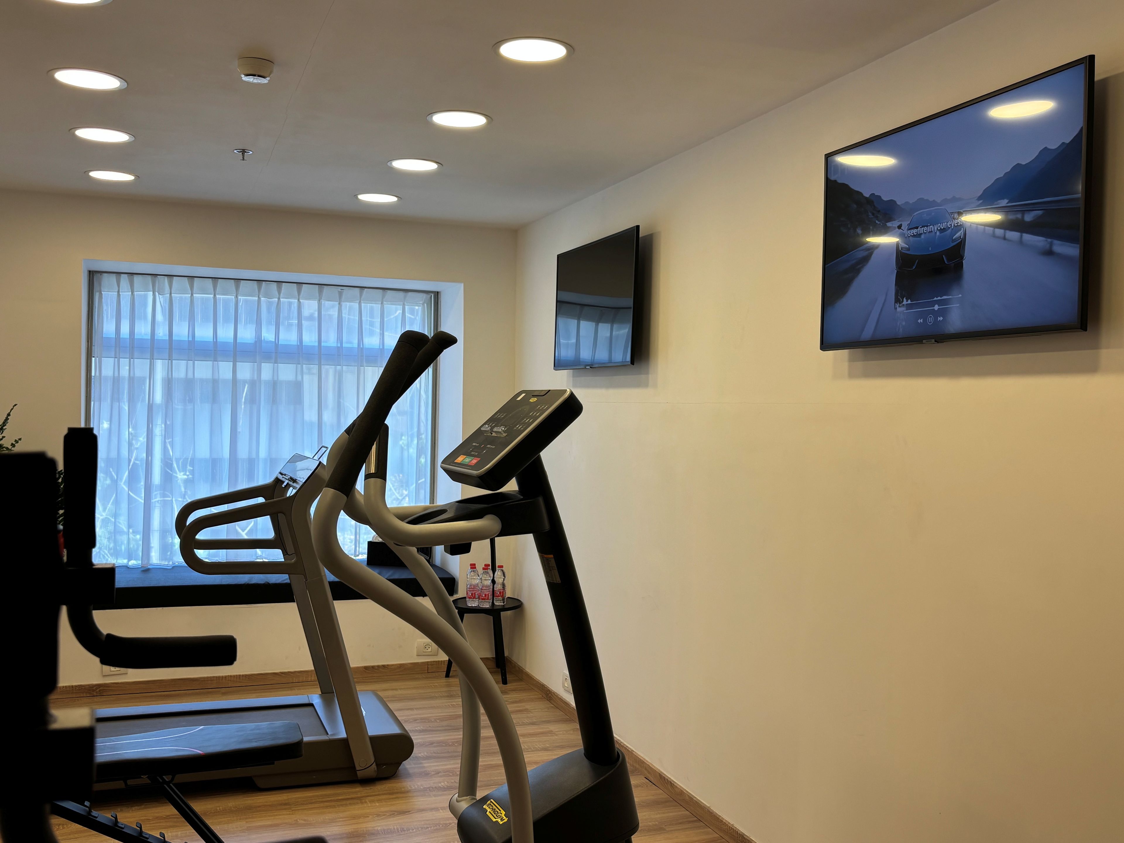 Une salle de sport à domicile équipée d’un tapis de course, d’un vélo elliptique et d’un téléviseur fixé au mur.