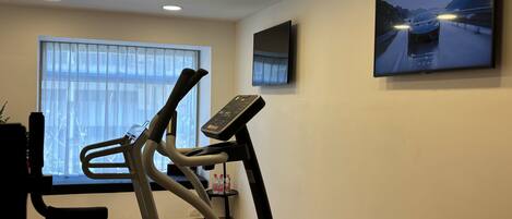 A home gym with a treadmill, elliptical, and a TV mounted on the wall.