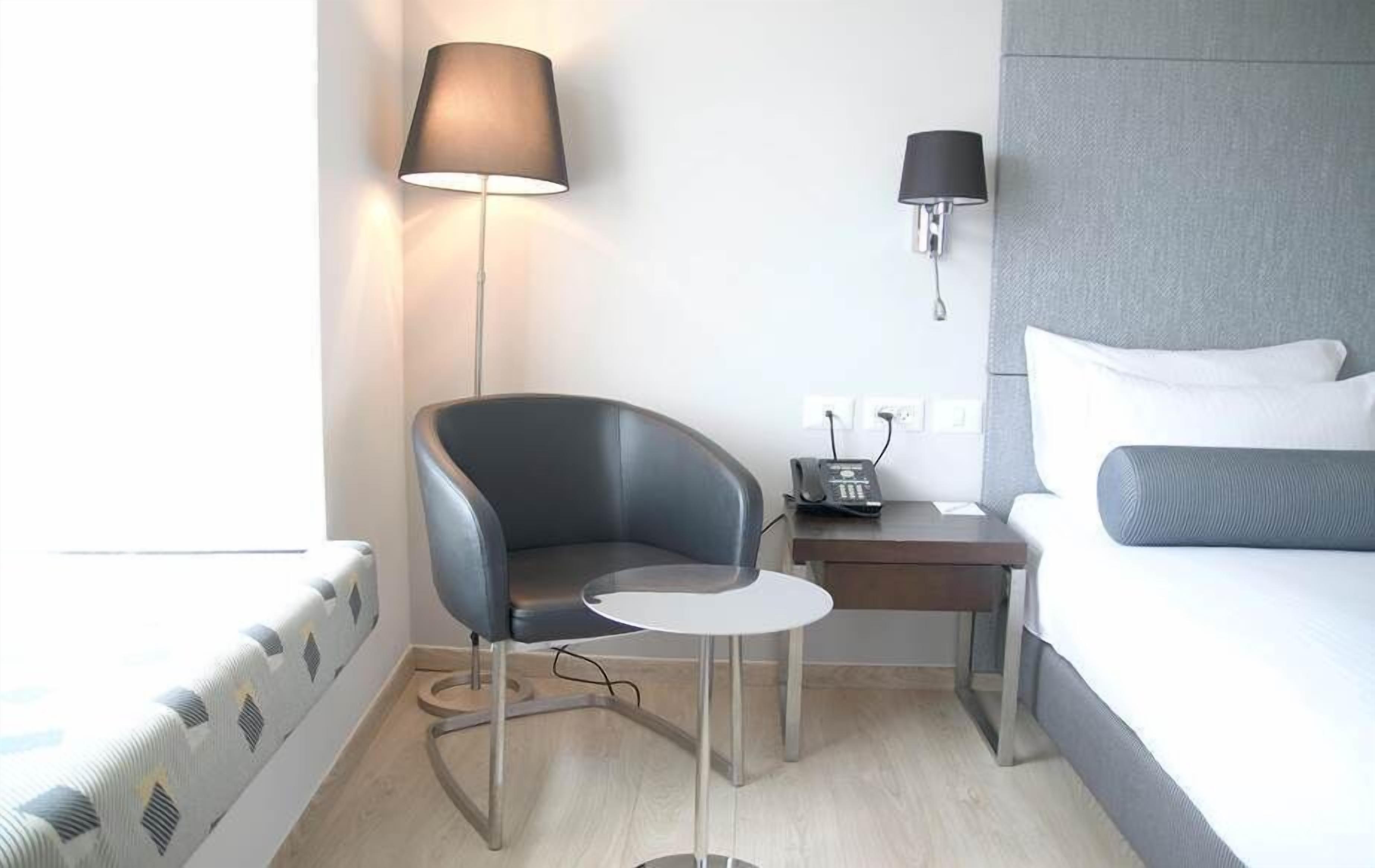 A modern hotel room with a bed, a desk, a chair, a lamp, and a phone.