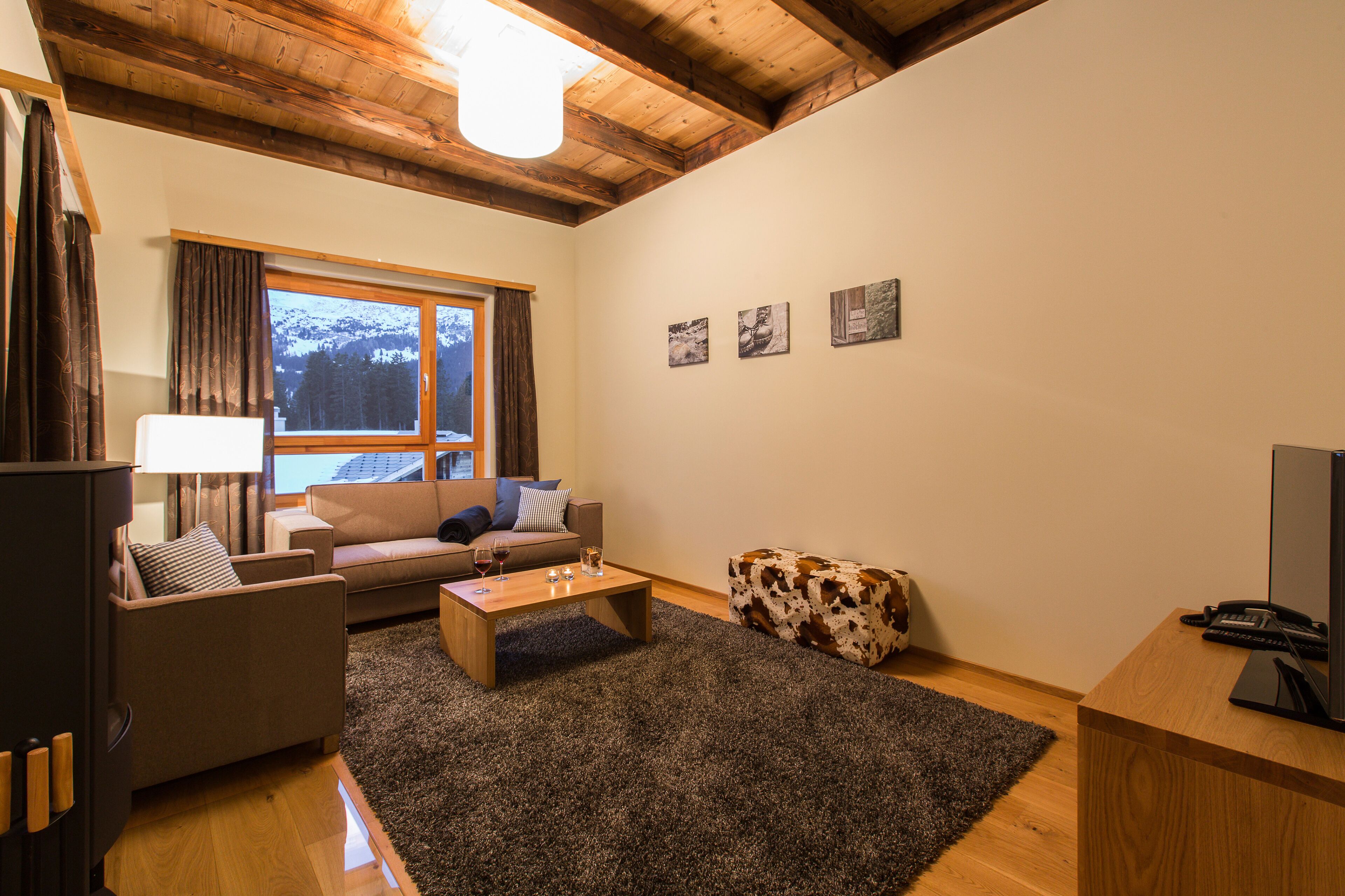 A living room with a wooden ceiling, a sofa, a coffee table, a television, and a window with curtains.