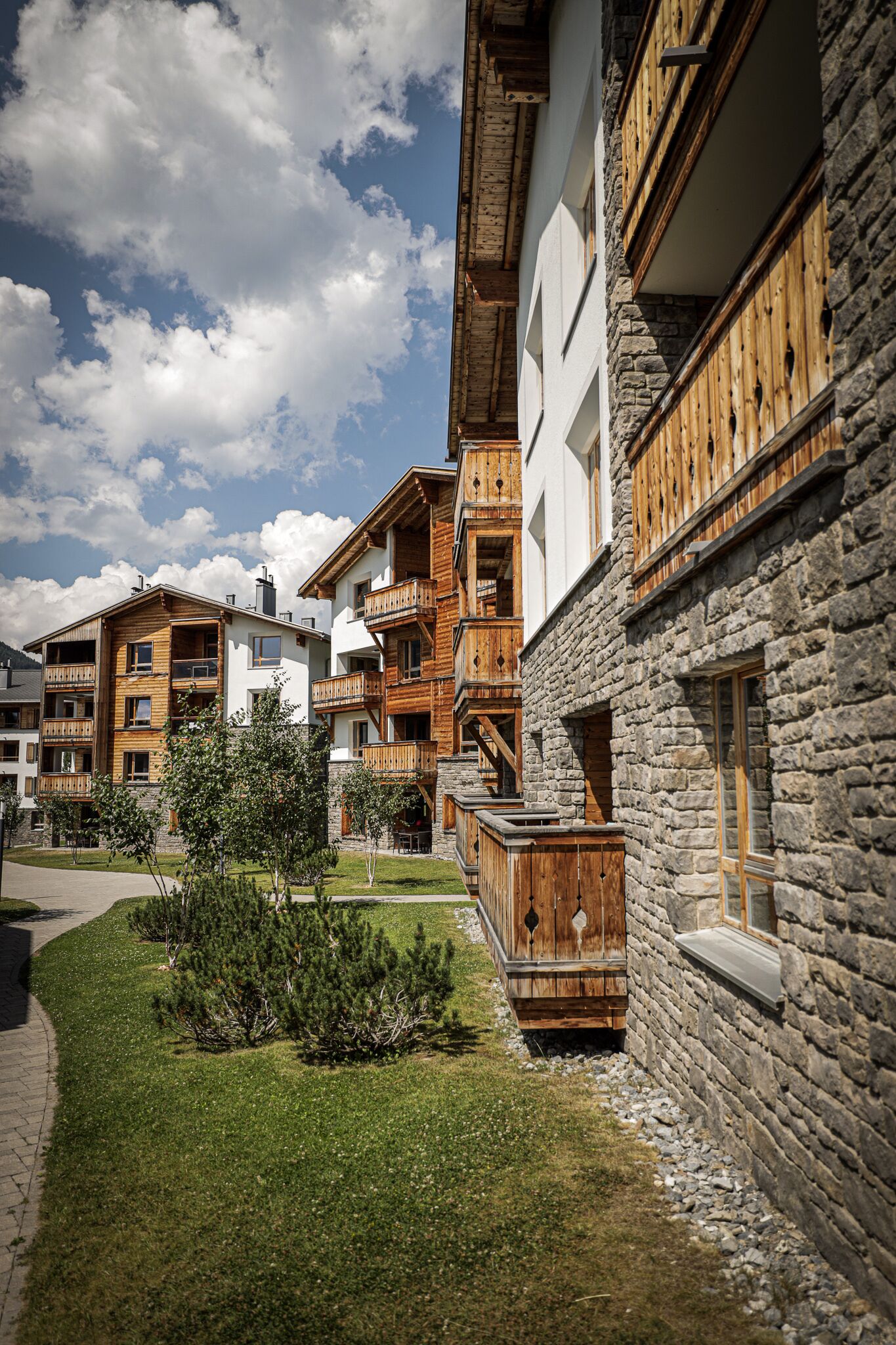 Une rangée d’immeubles à étages, dotés de balcons en bois et de façades en pierre, entourée d’une pelouse bien entretenue.
