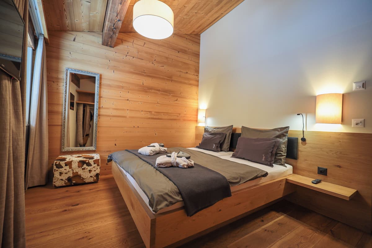 A wooden bedroom with a bed, bedside table, and a mirror.