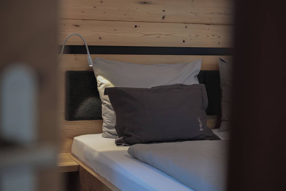 A bed with a wooden headboard, a bedside table, and a wall-mounted lamp.